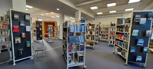 Bild vergrößern: Großer Raum der Bücherei mit gefüllten Bücherregalen, Drehständern, Sitzgelegenheit und einem Lesekorb.