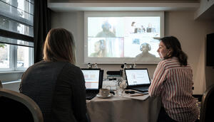 Bild vergrößern: Virtuelles Treffen der Projektkoordinatoren. Jessica Durstewitz und Rebecca Dienst sitzen am Laptop, auf einer Leinwand sind die Partner aus Tansania zu sehen, welche per Videochat zugeschaltet sind.