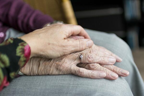 Bild vergrößern: Man sieht eine Hand einer Frau die liebevoll die Hände eines älteren Menschen ergreift.