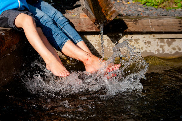 Bild vergrößern: Im Bild sieht man die Beine von einer Erwachsenen und einem Kind die im frischen Wasser des Rohrbach Tretbecken baden.