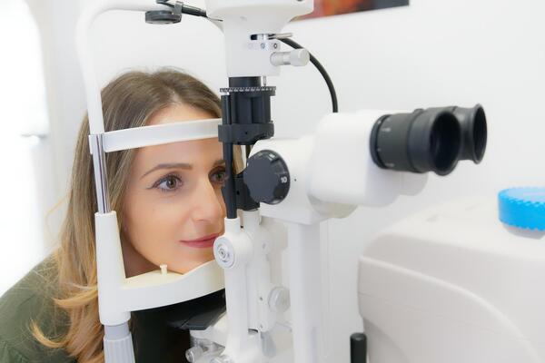 Bild vergrößern: Eine Patientin schaut durch ein Untersuchungsgerät bei einem Optiker.