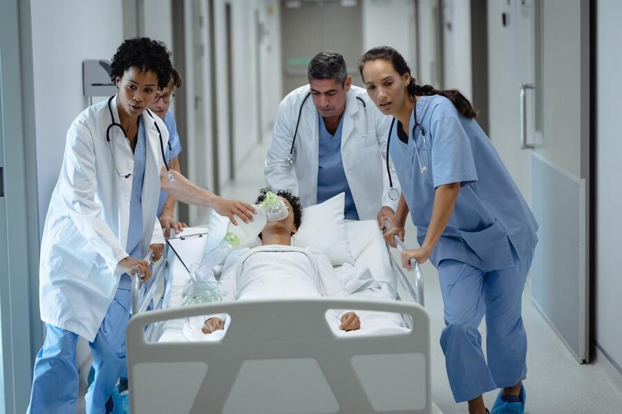 Bild vergrößern: Im Bild sieht man ein Team aus Ärzten und Pflegekräften, die einen Patienten in einem Krankenbett über den Flur schieben. Der Patient wird beatmet.