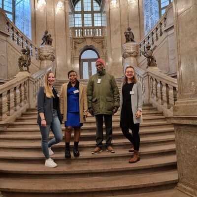 Bild vergrößern: Gruppenbild im Treppenhaus des Dresdner Rathauses. Zu sehen sind die Projektkoordinatorin und der Bürgermeister aus Tansania, sowie die beiden Projektkoordinatorinnen aus Bad Berleburg.
