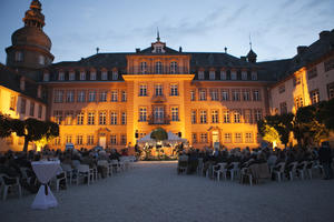 Bild vergrößern: Blick auf das Schloß Berleburg am Abend. Vor dem Schloss sieht man eine beleuchtete Bühne mit Musikern. Links und rechts vor der Bühne sind Sitzreihen mit Besuchern des Konzertes zu sehen.