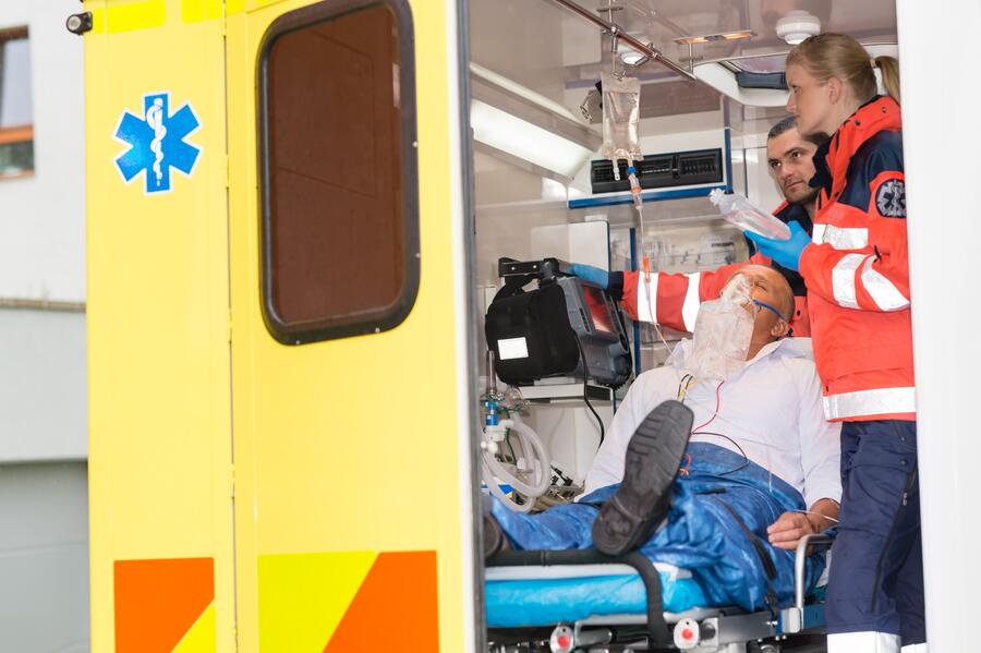 Bild vergrößern: Im Bild sieht man einen Patienten der im Rettungswagen aufgenommen wurde. Er wird von zwei Rettungssanitätern versorgt.