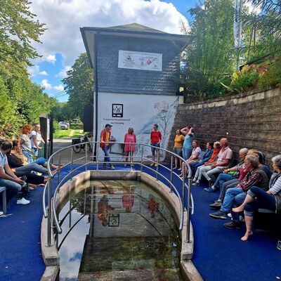 Bild vergr&ouml;&szlig;ern: Im Bild sieht man sehr viele Teilnehmer*innen am Tretbecken an der Espe-Quelle. Die Besucher sitzen auf B&auml;nken rund um das Tretbecken und verfolgen den Vortrag des Referenten zu den Kneipp schen Wasseranwendungen.