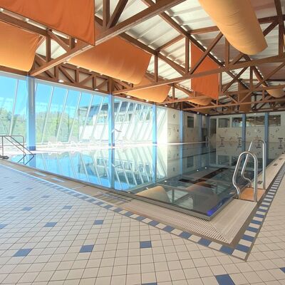 Bild vergr&ouml;&szlig;ern: Im Bild sieht man das gro&szlig;e Schwimmbecken des Rothaarbades mit Blick auf die gro&szlig;e Glasfront nach drau&szlig;en. Vor den Fenstern stehen Ruheliegen.