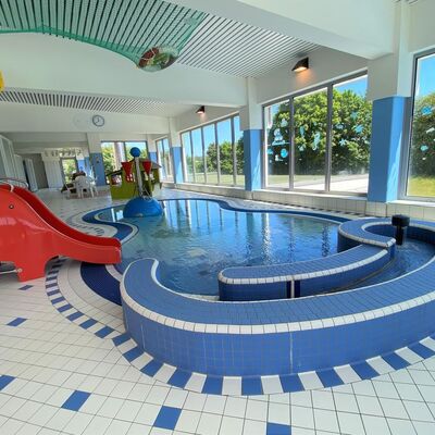 Bild vergr&ouml;&szlig;ern: Im Bild sieht man das Kinderbecken in den Farben blau und weiss und auf der linken Seite eine rote Rutsche die ins Becken f&uuml;hrt.