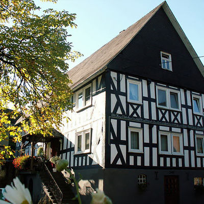 Bild vergrößern: Ein typisches wittgensteiner Fachwerkhaus mit seitlichem Treppenaufgang und einem alten Laubbaum.