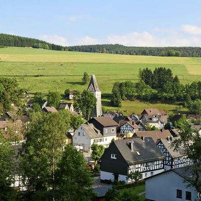 Bild vergrößern: Am Fuße des eines grünen Hangs liegt die Ortschaft Girkhausen mit malerischen Fachwerkhäusern