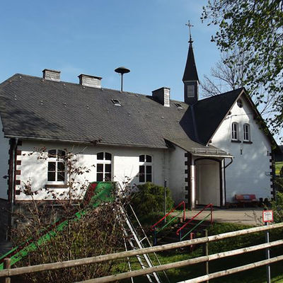 Bild vergrößern: Das Hemschlarer Dorfgemeinschaftshaus liegt direkt am Kinderspielplatz. Es ragt ein Turm mit Kreuz in dem Himmel.