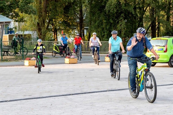 Bild vergrößern: Fünf erwachsene Personen fahren hintereinander weg mit Fahrrädern. Links daneben fährt ein Junge auf einem Fahrrad. Die Person auf dem vordersten Fahrrad ist Bernd Fuhrmann. Er winkt mit seiner Hand in die linke Richtung.