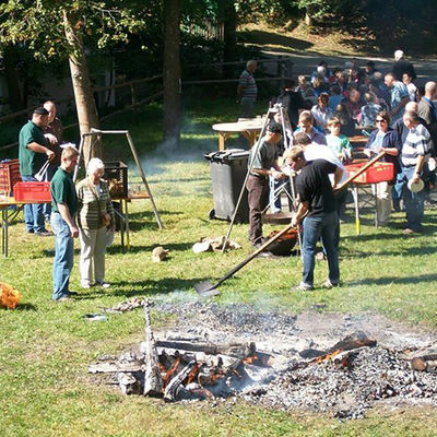 Bild vergrößern: Dorfbewohner feiern ein Grillfest. Im Vordergrund ist eine Feuerstelle zu sehen.