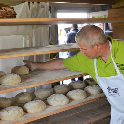 Bild vergrößern: Im Wunderthäuser Backhaus liegen mehrere frische Brote in Regalen. Der Bäcker sortiert weitere Ware dazu.