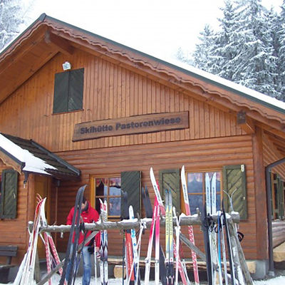 Bild vergrößern: Vor dem Holzgebäude der Wunderthäuser Skihütte Pastorenwiese stehen einige Paar Ski bereit.